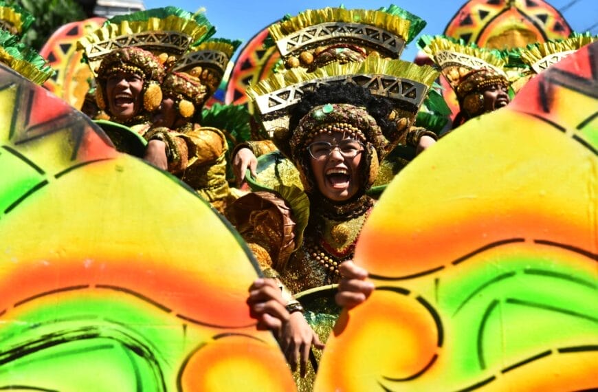 Dancers in colorful, ornate costumes with vibrant green and yellow designs perform energetically at the Diyandi Festival.