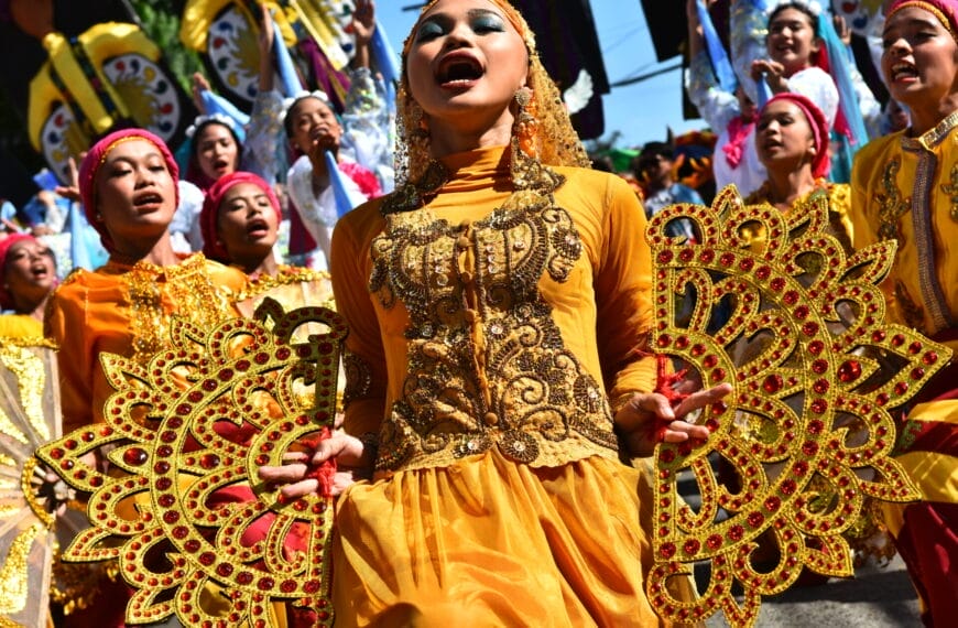 Dancers in vibrant yellow costumes and headpieces perform energetically with ornate props at the Diyandi Festival.