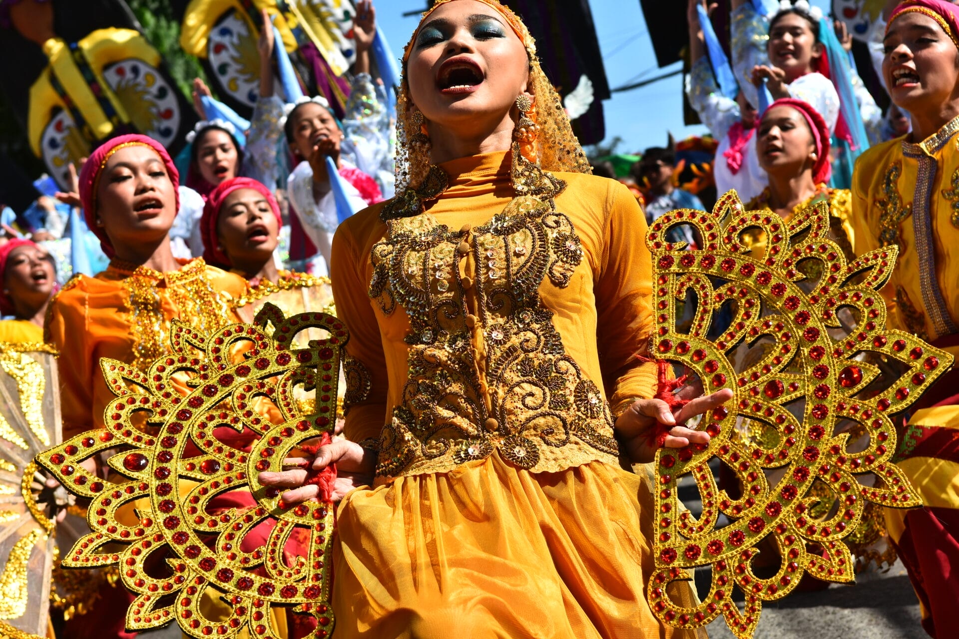 Dancers in vibrant yellow costumes and headpieces perform energetically with ornate props at the Diyandi Festival.