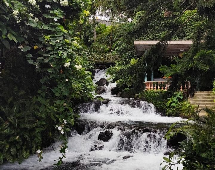 Cascading Iligan City waterfalls surrounded by lush greenery and a small gazebo on the right.