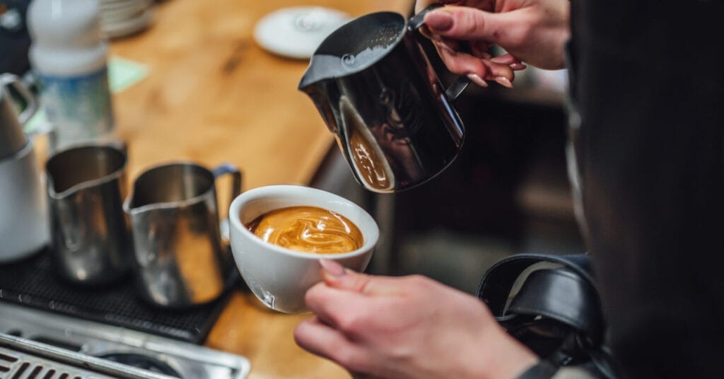 barista in an iligan coffee shop pours milk into espresso, crafting perfect latte art on a wooden counter.