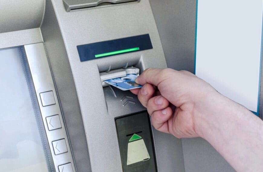 hand inserting a card into an iligan atm, with buttons and a green light indicator above the card slot.