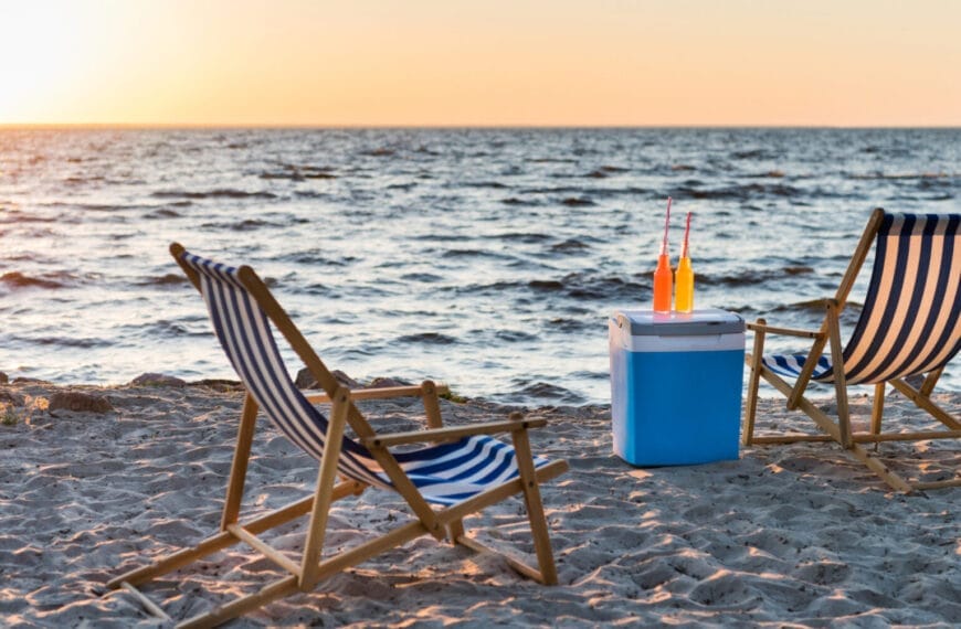 Two striped beach chairs on Iligans sandy shore, a cooler with orange drinks, ocean waves, and sunset sky.