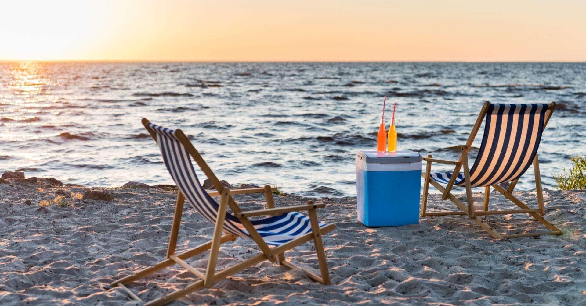 Two striped beach chairs on Iligans sandy shore, a cooler with orange drinks, ocean waves, and sunset sky.