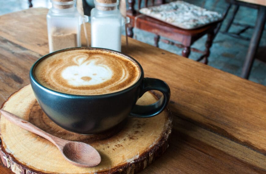 Latte art of a rabbit in a dark cup at Iligan Coffee, with sugar jars and a chair on a wooden coaster.