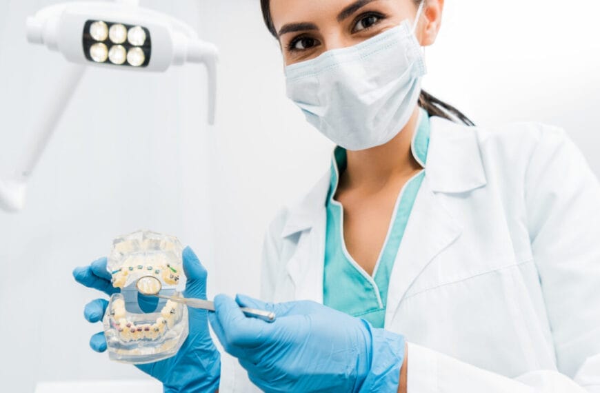 quality dental care from a dentist in mask and scrubs, holding a mold and tool under the light.