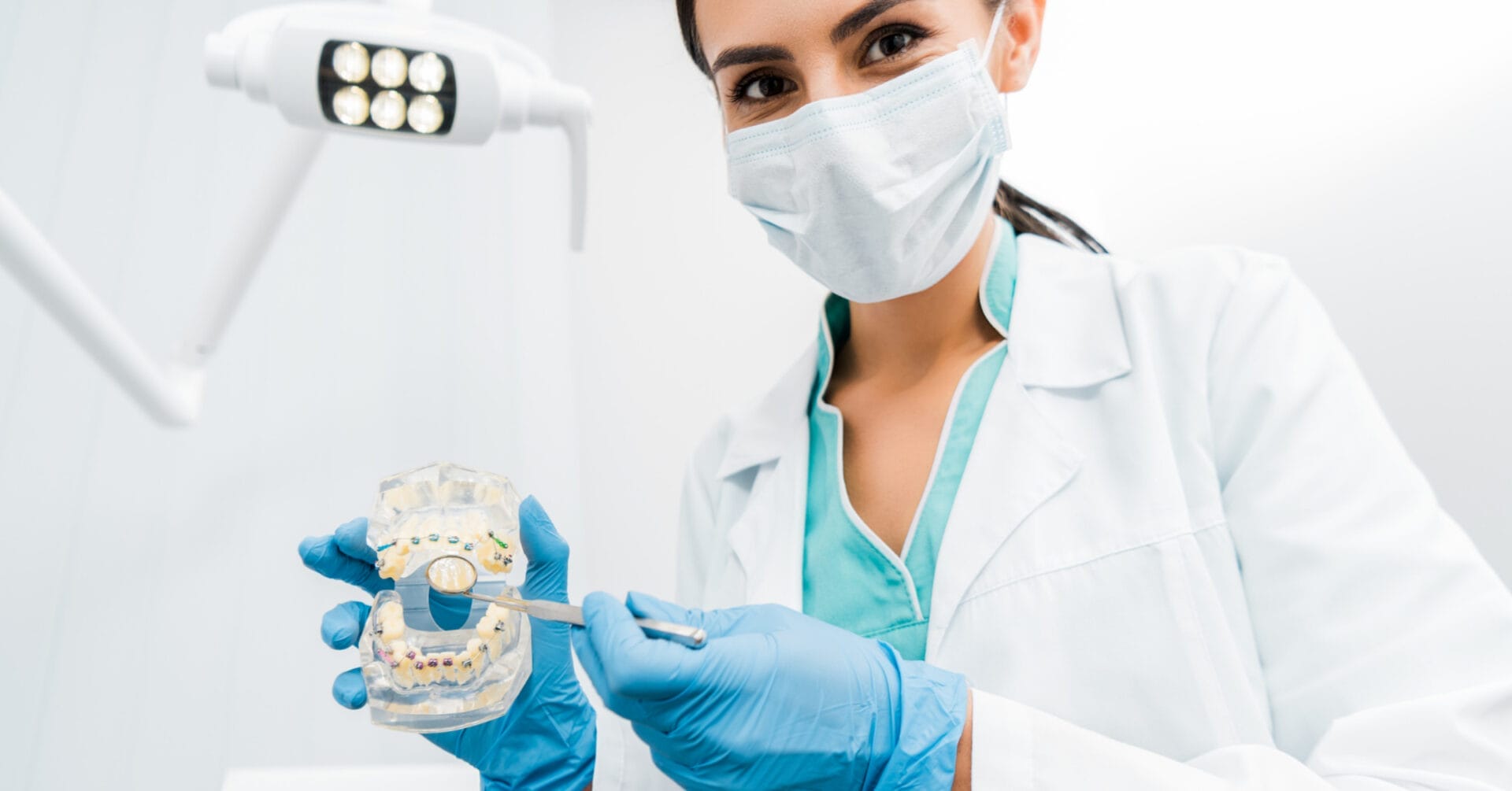 quality dental care from a dentist in mask and scrubs, holding a mold and tool under the light.