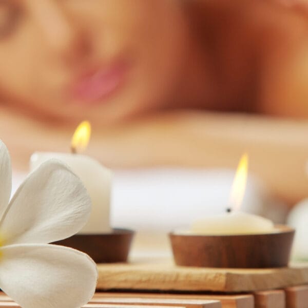 Close-up of lit candles and a white flower, setting the tranquil mood for an Iligan massage in the background.