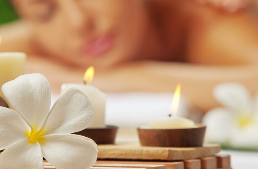 Close-up of lit candles and a white flower, setting the tranquil mood for an Iligan massage in the background.