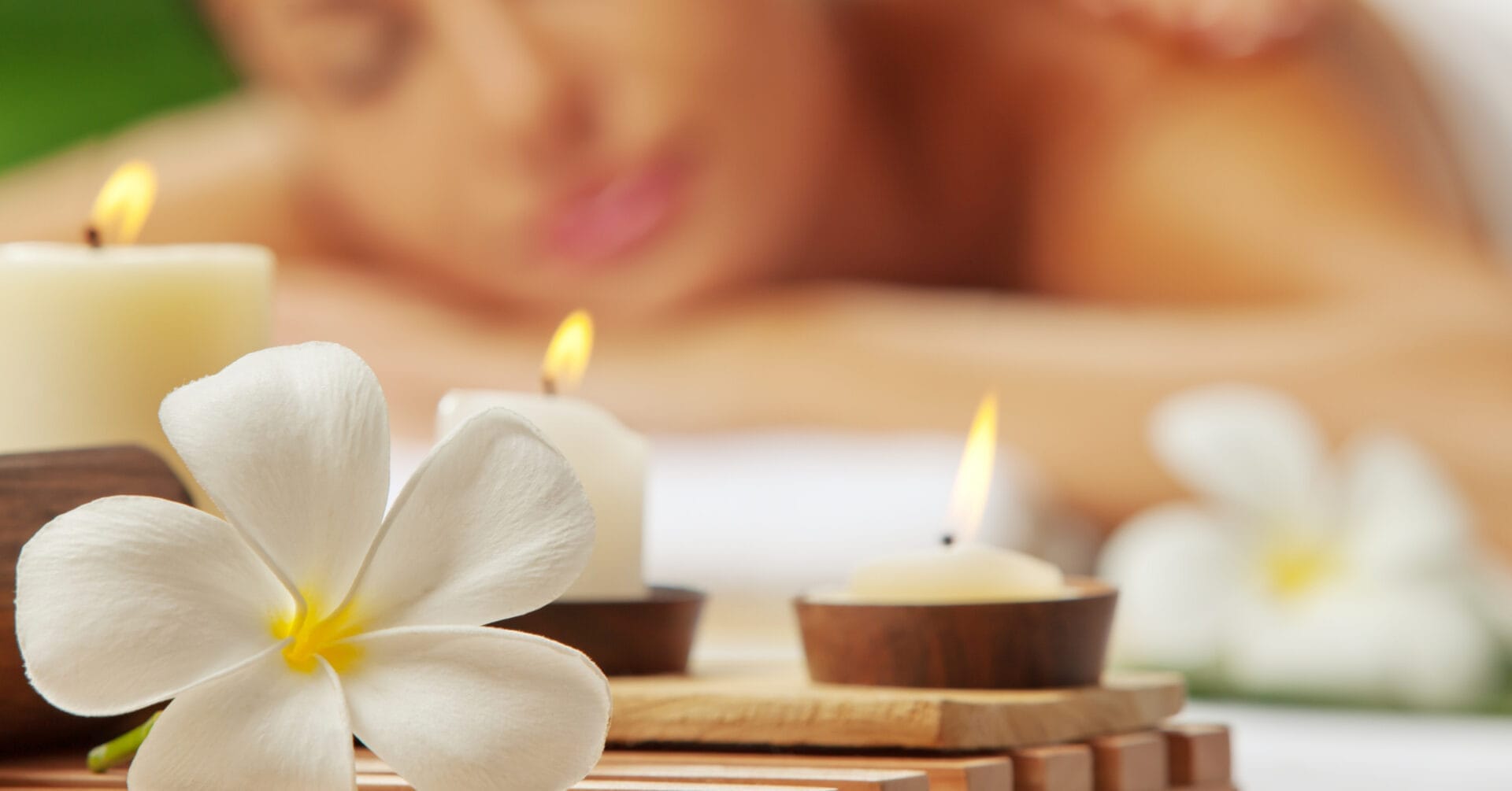 Close-up of lit candles and a white flower, setting the tranquil mood for an Iligan massage in the background.