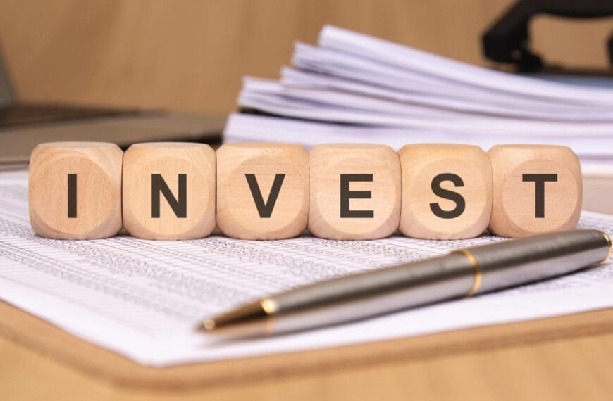 Wooden blocks spelling INVEST ILIGAN on papers with a pen and stacked files in the background.