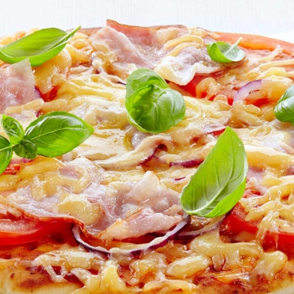 Iligan pizza topped with sliced tomatoes, ham, melted cheese, and fresh basil leaves on a white background.