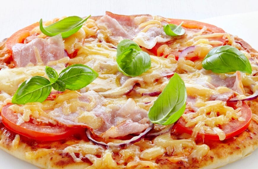 Iligan pizza topped with sliced tomatoes, ham, melted cheese, and fresh basil leaves on a white background.