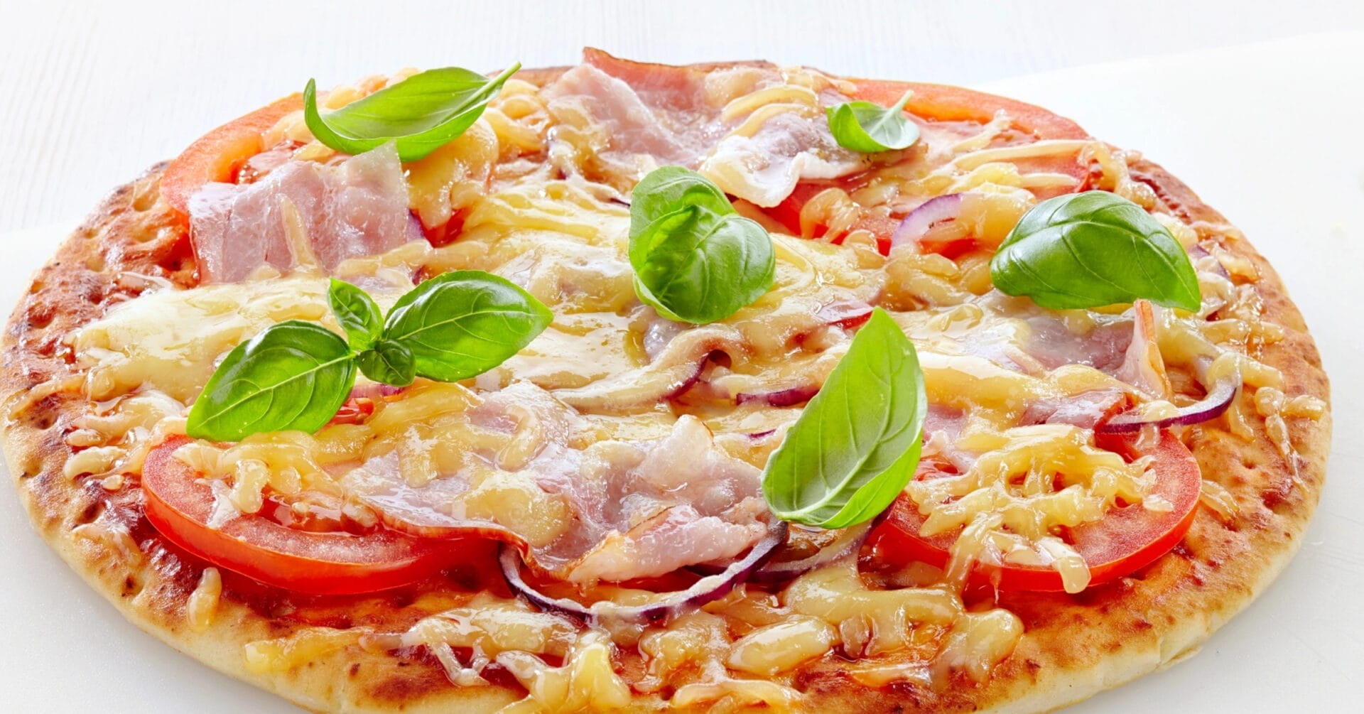 Iligan pizza topped with sliced tomatoes, ham, melted cheese, and fresh basil leaves on a white background.